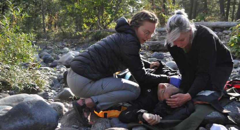 three people participate in a wilderness first responder exercise